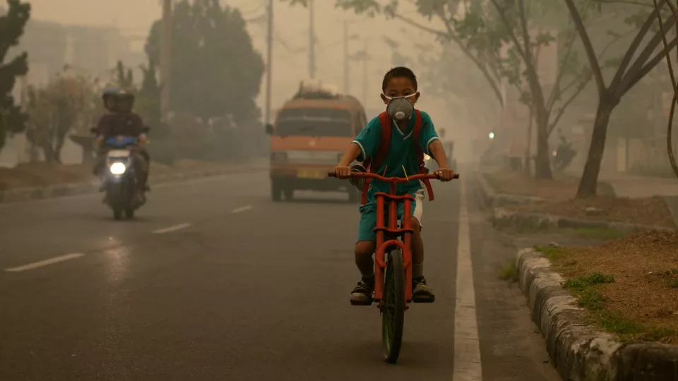 Indonesisk pojke som cyklar genom avgaser, på väg till skolan. Fotograf: Aulia Erlangga